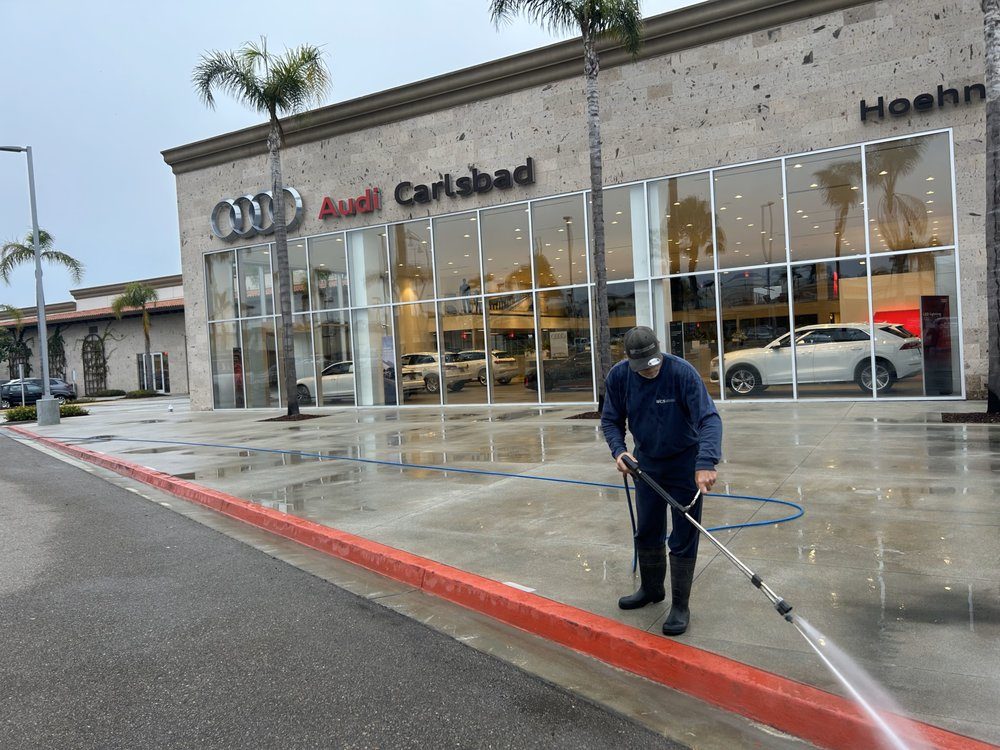 West Coast Services technician pressure washing the lot in front of the Audi Carlsbad showroom glass