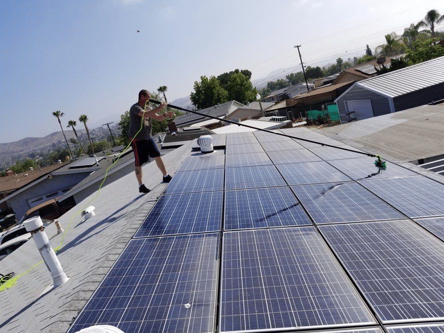 Technician cleaning a rooftop solar array with a water-fed pole